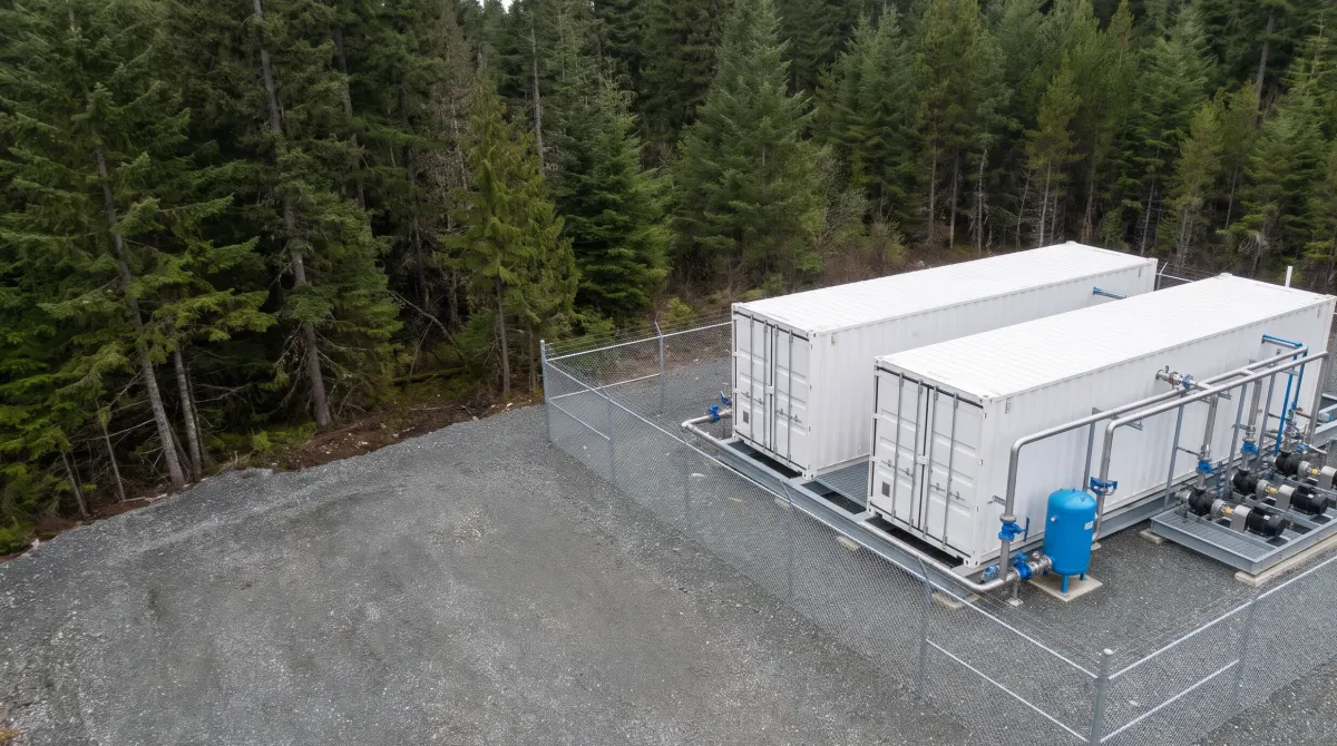 A containerised package treatment plant on a gravel site beside a forest